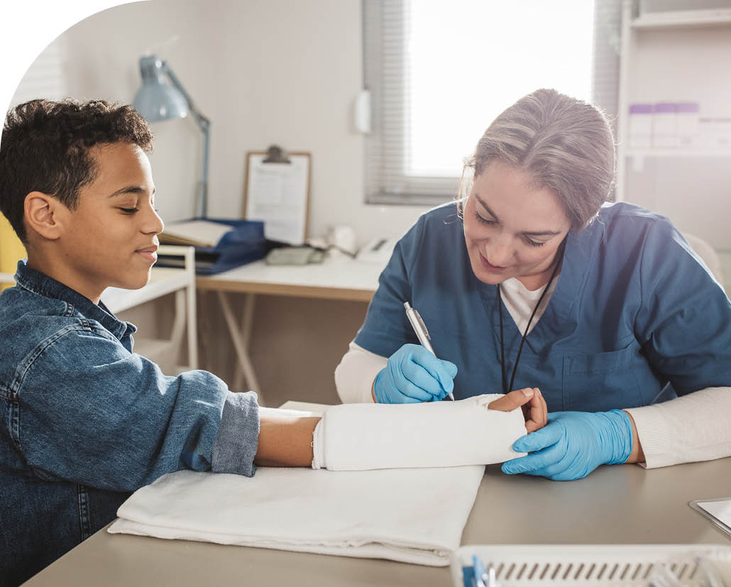 Young boy with broken arm wearing cast, doctor examining his injury